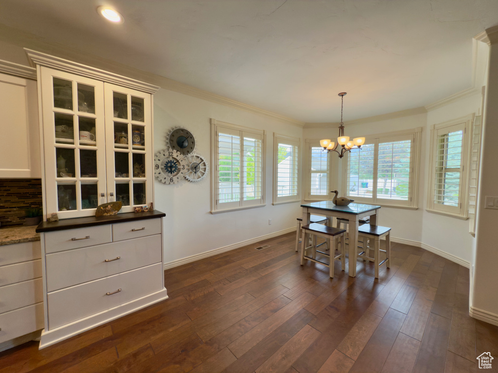 Dining area featuring a chandelier, plenty of natural light, baseboards, dark wood-style flooring, and crown molding