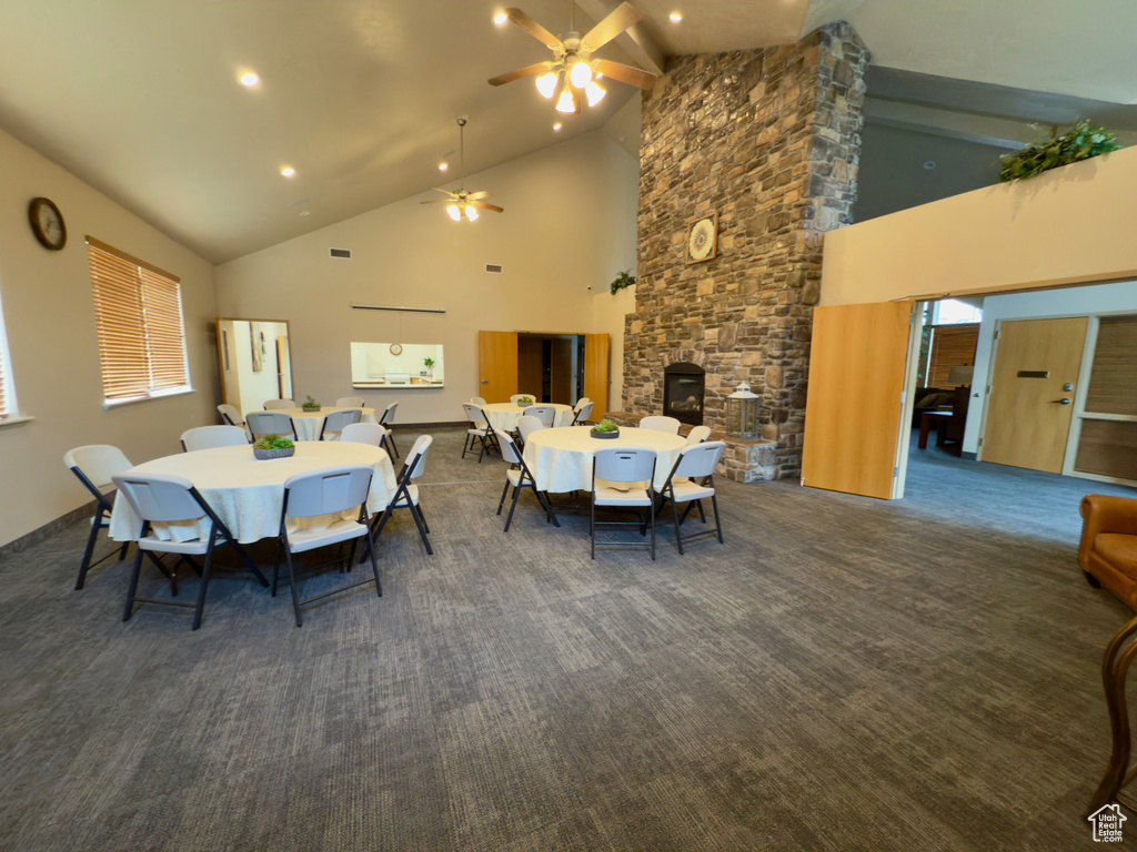 Carpeted dining area with high vaulted ceiling, a ceiling fan, beam ceiling, recessed lighting, and a stone fireplace