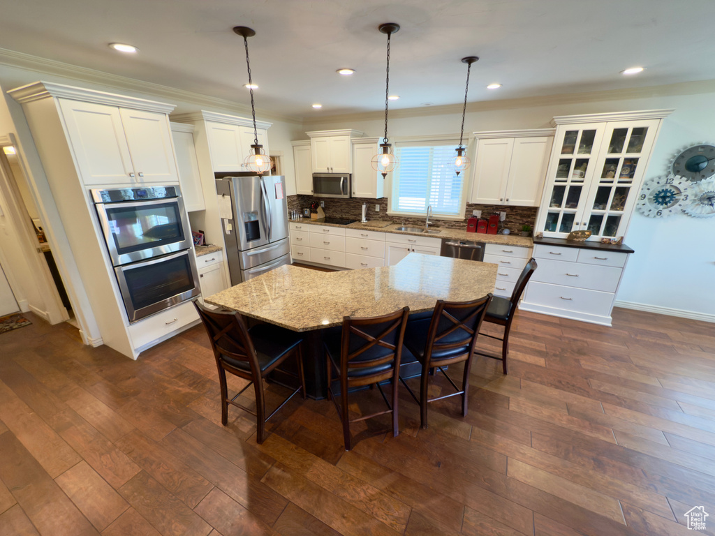 Kitchen with appliances with stainless steel finishes, a sink, a kitchen bar, white cabinets, and tasteful backsplash