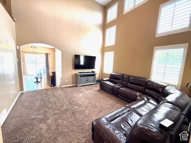 Carpeted living area featuring a towering ceiling, arched walkways, and baseboards