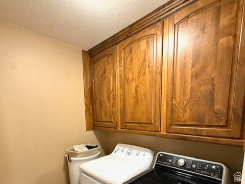 Washroom with cabinet space, washing machine and clothes dryer, light tile patterned flooring, baseboards, and a textured ceiling