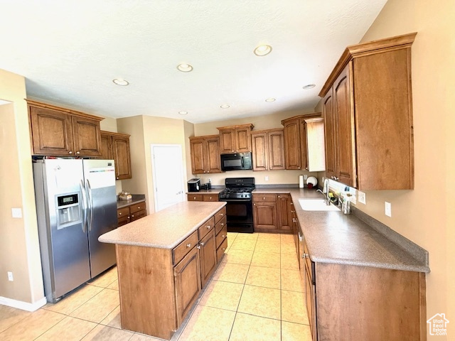 Kitchen with black appliances, a center island, a sink, light tile patterned flooring, and brown cabinetry