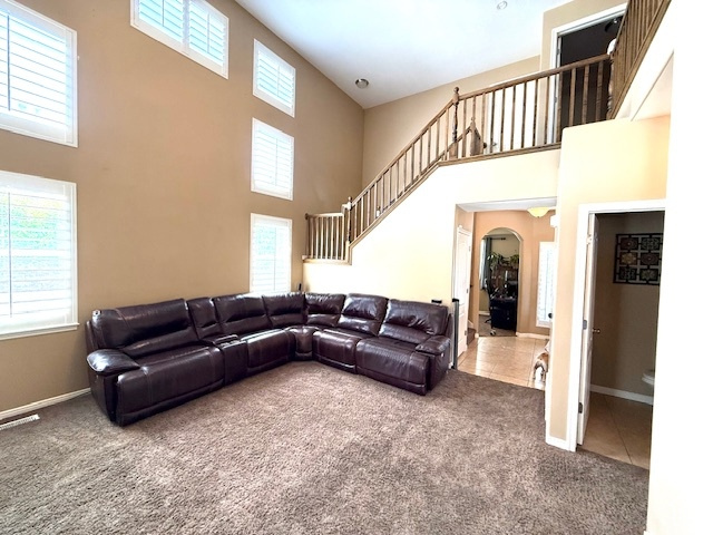 Carpeted living area featuring a high ceiling, stairs, plenty of natural light, and baseboards