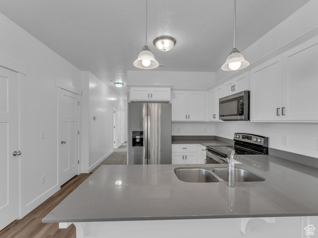 Kitchen with stainless steel appliances, a sink, a peninsula, white cabinets, and dark countertops