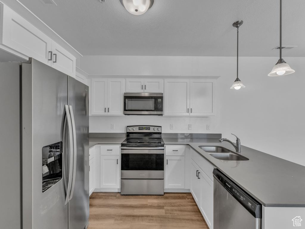 Kitchen with stainless steel appliances, a sink, a peninsula, light wood finished floors, and white cabinets