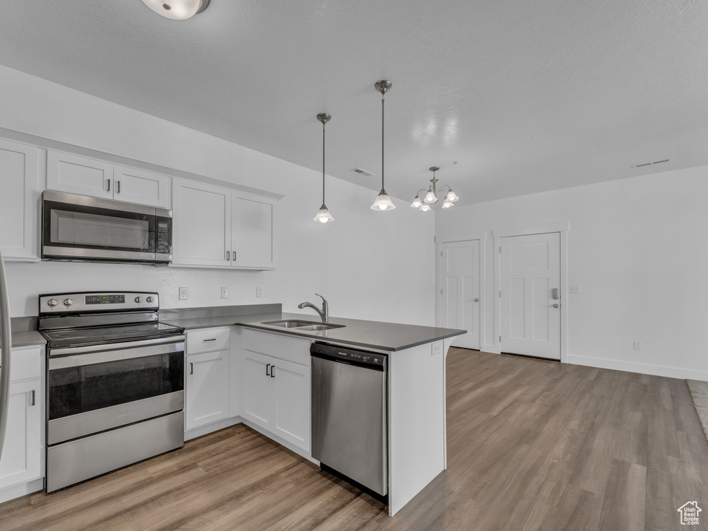 Kitchen with appliances with stainless steel finishes, a sink, light wood-style floors, and white cabinets