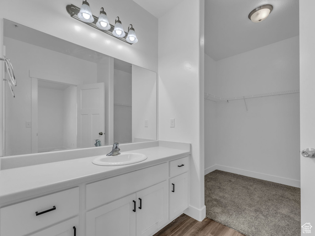 Bathroom featuring vanity, a walk in closet, baseboards, and wood finished floors