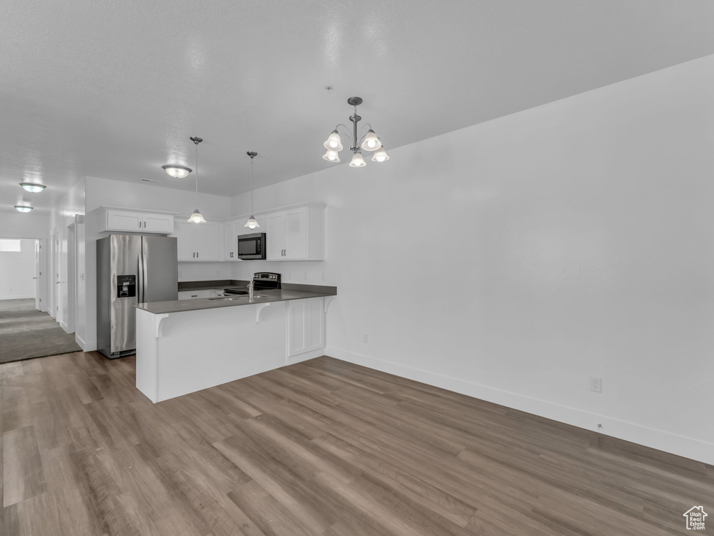 Kitchen with stainless steel appliances, a peninsula, white cabinets, dark wood-type flooring, and baseboards