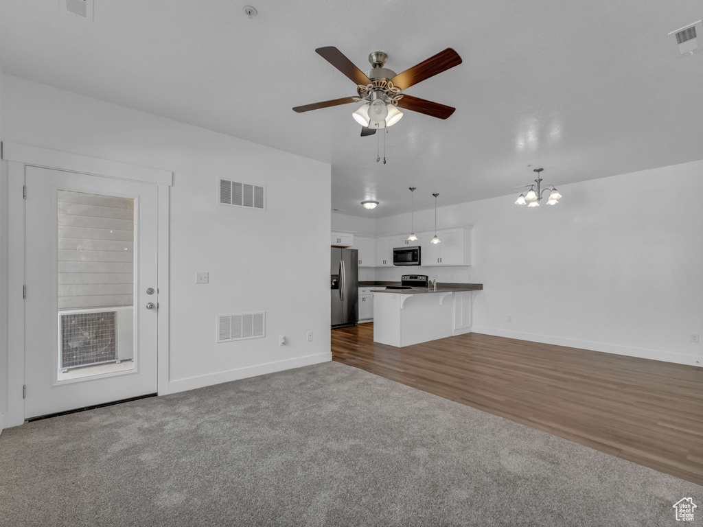 Unfurnished living room with baseboards, ceiling fan, dark colored carpet, and a chandelier