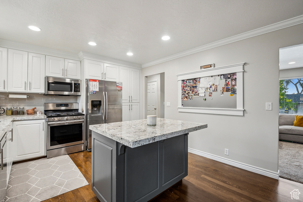 Kitchen featuring stainless steel appliances, crown molding, white cabinets, dark wood-style flooring, and a kitchen island