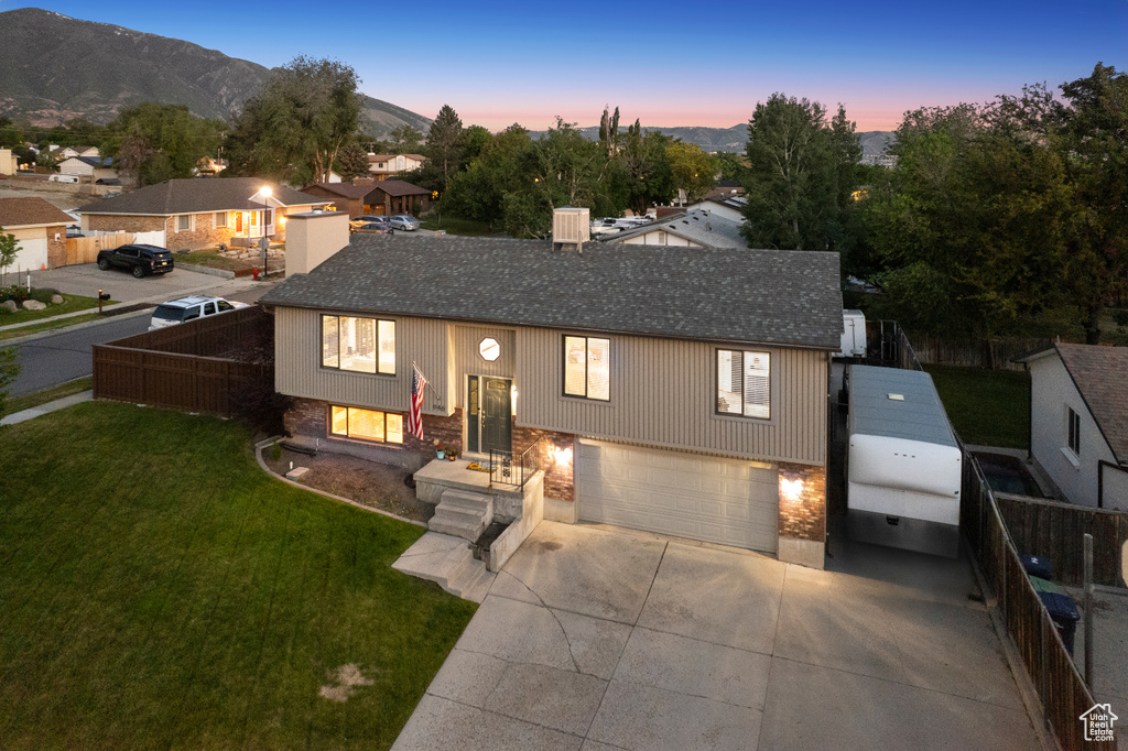 Bi-level home with an attached garage, a shingled roof, concrete driveway, and a mountain view