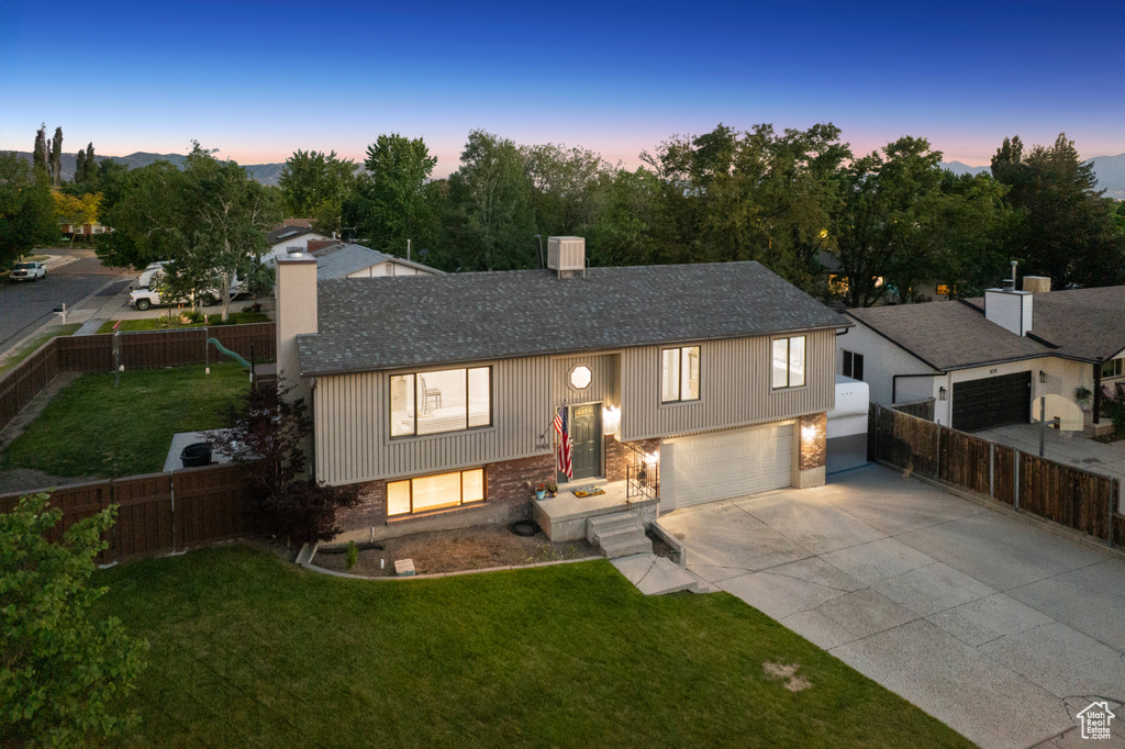Raised ranch with a chimney, driveway, roof with shingles, and an attached garage