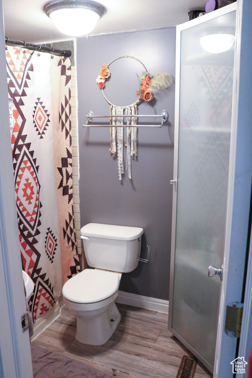 Full bathroom featuring toilet, wood finished floors, baseboards, and curtained shower