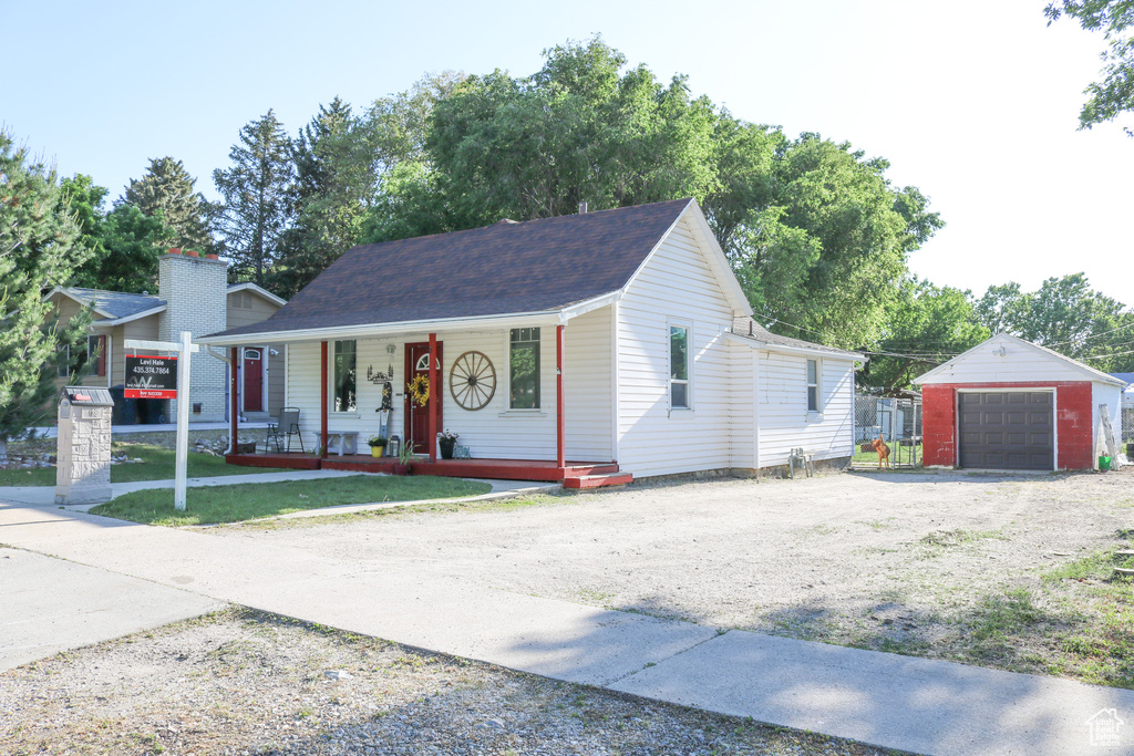 View of front of property with covered porch, dirt driveway, a detached garage, an outdoor structure, and roof with shingles