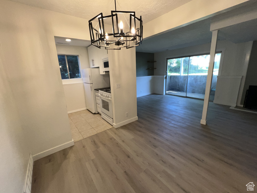 Unfurnished dining area featuring a chandelier, wood finished floors, baseboards, and a textured ceiling