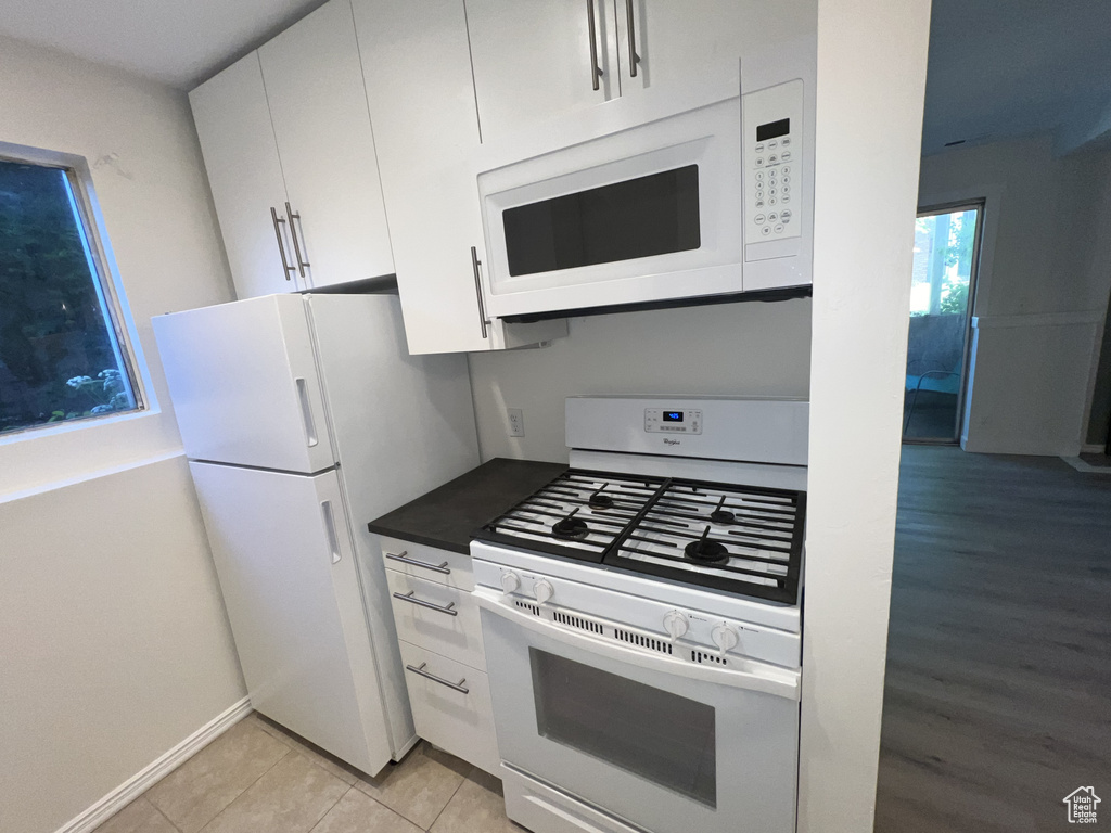 Kitchen with white appliances, white cabinetry, dark countertops, baseboards, and light tile patterned flooring