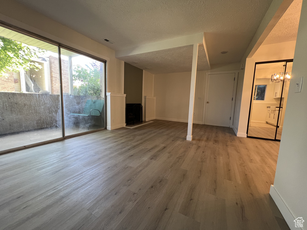 Unfurnished living room with a textured ceiling, a fireplace with raised hearth, wood finished floors, baseboards, and a chandelier