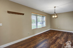 Spare room with a chandelier, dark wood-style floors, and baseboards