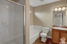 Bathroom featuring a stall shower, vanity, a garden tub, toilet, and wood finished floors