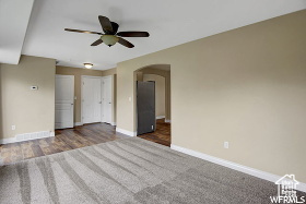 Carpeted empty room featuring arched walkways, baseboards, and ceiling fan