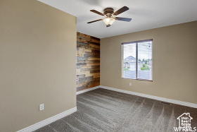 Empty room featuring baseboards, wood walls, dark colored carpet, and an accent wall
