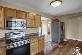 Kitchen featuring appliances with stainless steel finishes, arched walkways, dark countertops, and dark wood finished floors