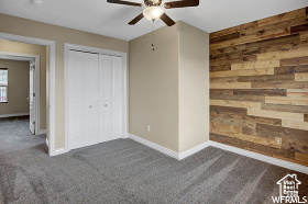Unfurnished bedroom with carpet flooring, baseboards, wooden walls, a closet, and a ceiling fan