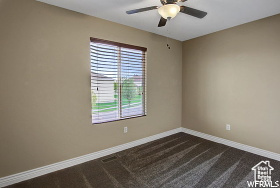 Unfurnished room with a ceiling fan, baseboards, and dark carpet