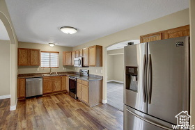 Kitchen with appliances with stainless steel finishes, arched walkways, dark wood finished floors, baseboards, and a sink
