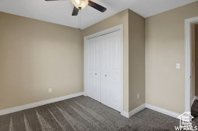 Unfurnished bedroom with dark colored carpet, a closet, baseboards, and a ceiling fan