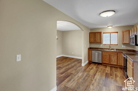 Kitchen featuring appliances with stainless steel finishes, arched walkways, wood finished floors, baseboards, and a sink