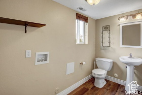 Bathroom featuring toilet, wood finished floors, baseboards, and a sink