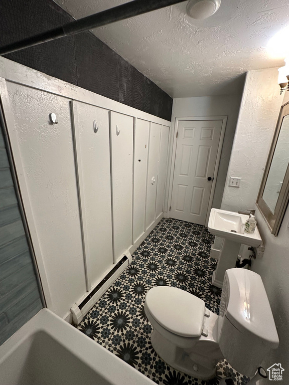 Full bathroom featuring toilet, a baseboard radiator, a textured wall, a textured ceiling, and a bathtub
