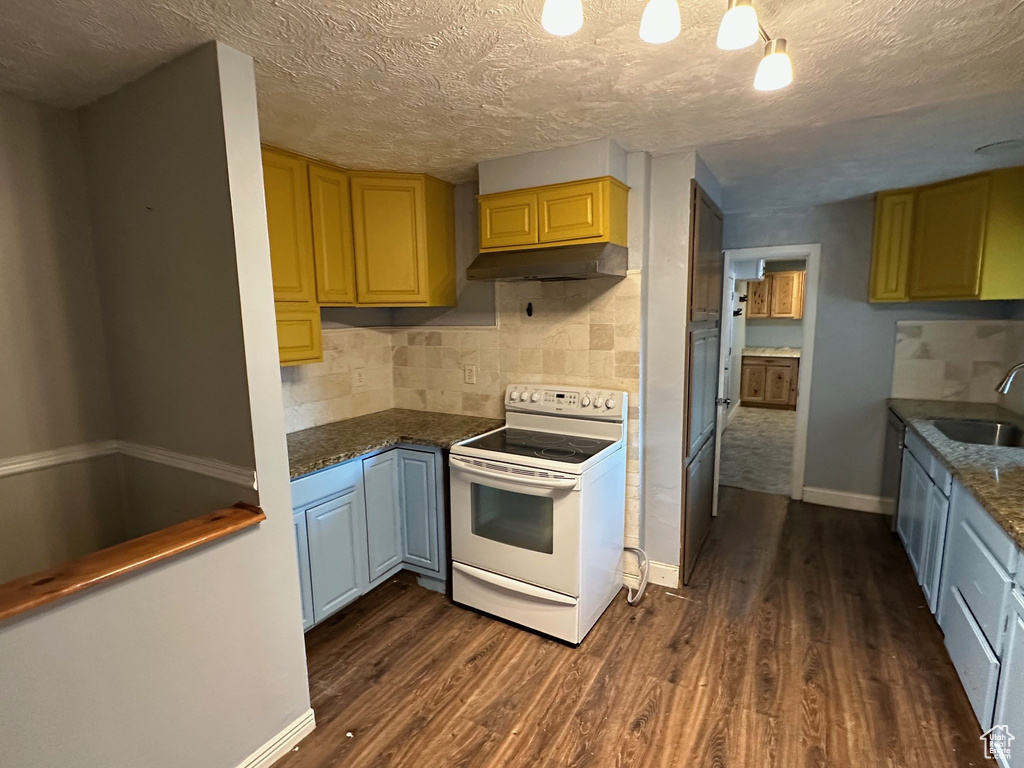 Kitchen with white electric range, dark wood finished floors, baseboards, under cabinet range hood, and a textured ceiling