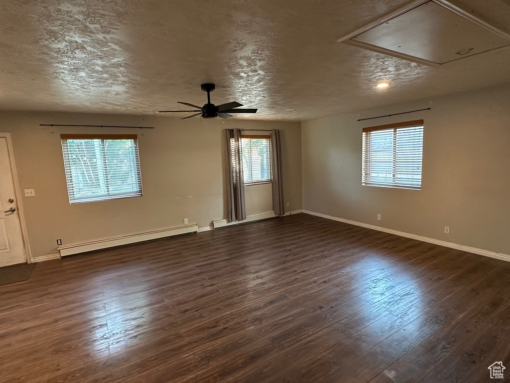 Spare room featuring baseboard heating, baseboards, dark wood-style floors, attic access, and a textured ceiling