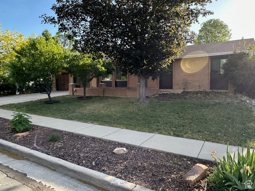 View of front of home with a front yard, brick siding, concrete driveway, and an attached garage