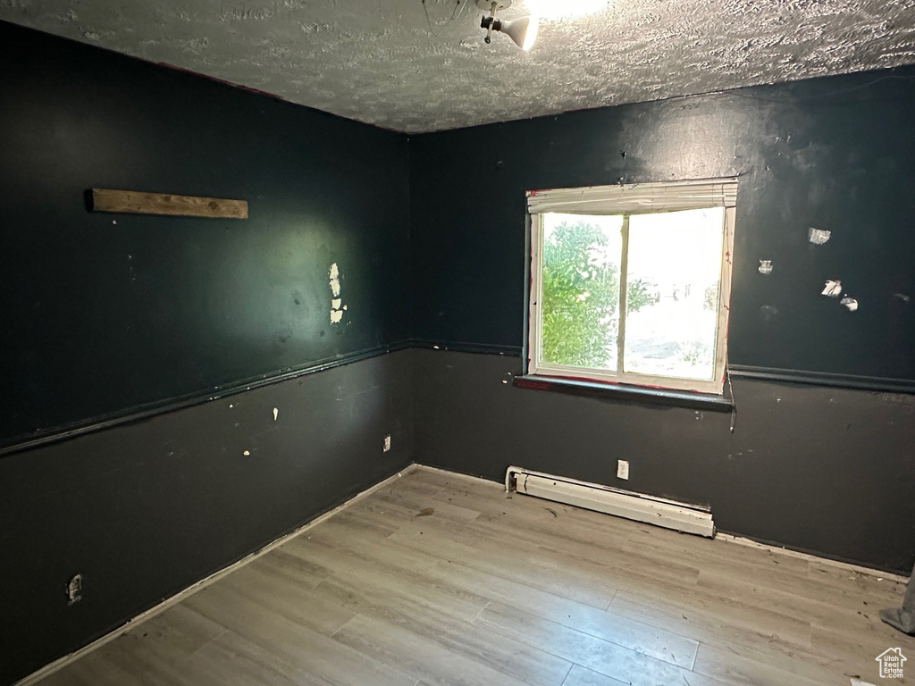 Empty room with a baseboard heating unit, wood finished floors, and a textured ceiling