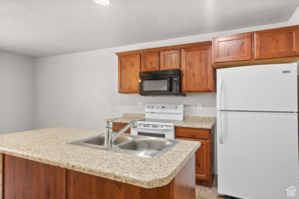 Kitchen featuring white appliances, a sink, light countertops, brown cabinetry, and a kitchen island with sink