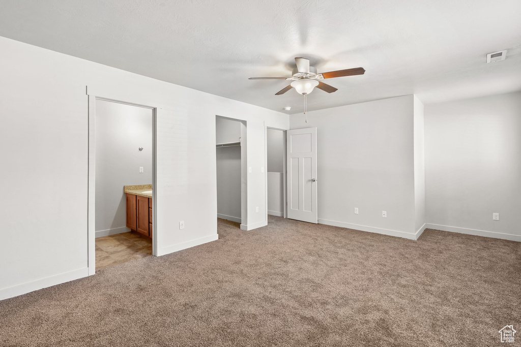 Unfurnished bedroom with light carpet, connected bathroom, a spacious closet, baseboards, and a ceiling fan
