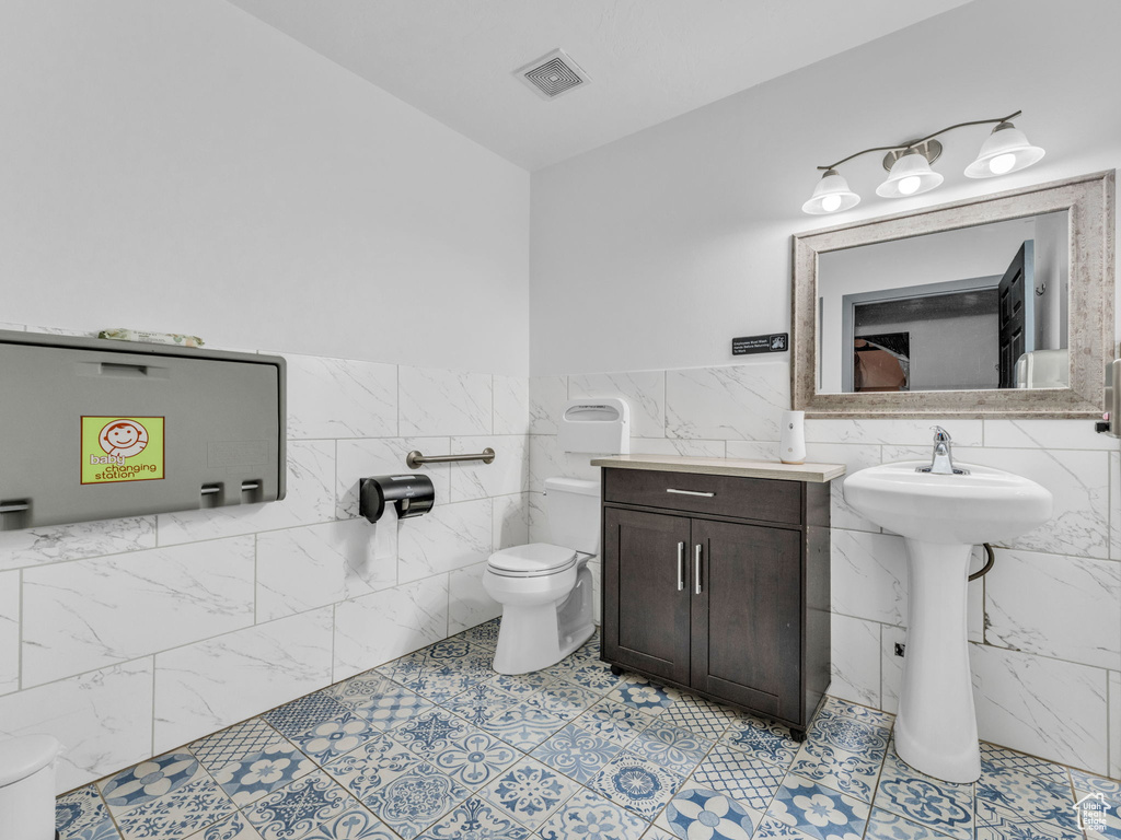 Bathroom with toilet, tile walls, a wainscoted wall, and a sink
