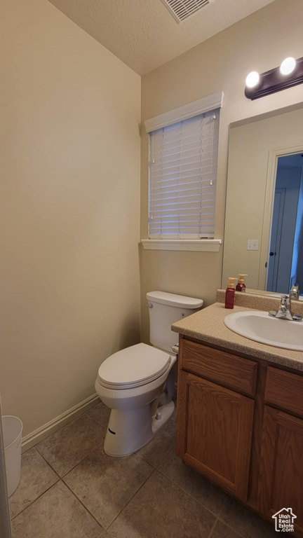 Half bath with toilet, tile patterned floors, vanity, and a textured ceiling