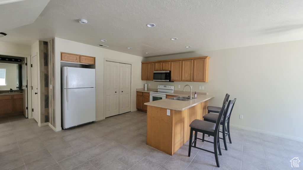 Kitchen with white appliances, a sink, a peninsula, light countertops, and a textured ceiling