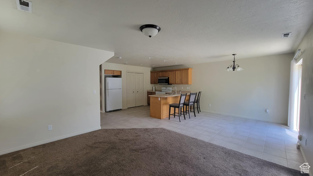 Kitchen with freestanding refrigerator, stainless steel microwave, a kitchen bar, a chandelier, and light tile patterned floors