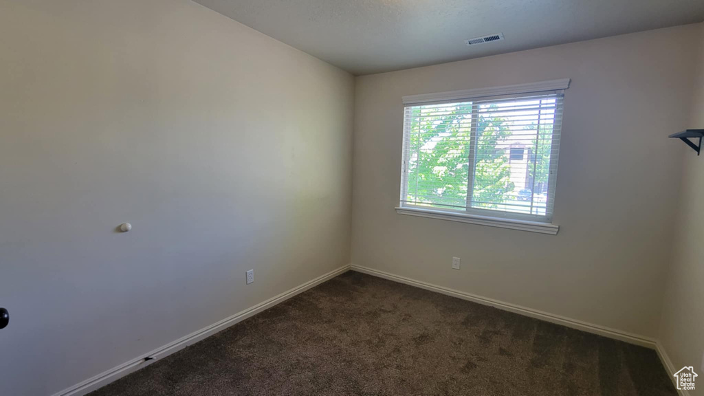Spare room featuring dark colored carpet and baseboards
