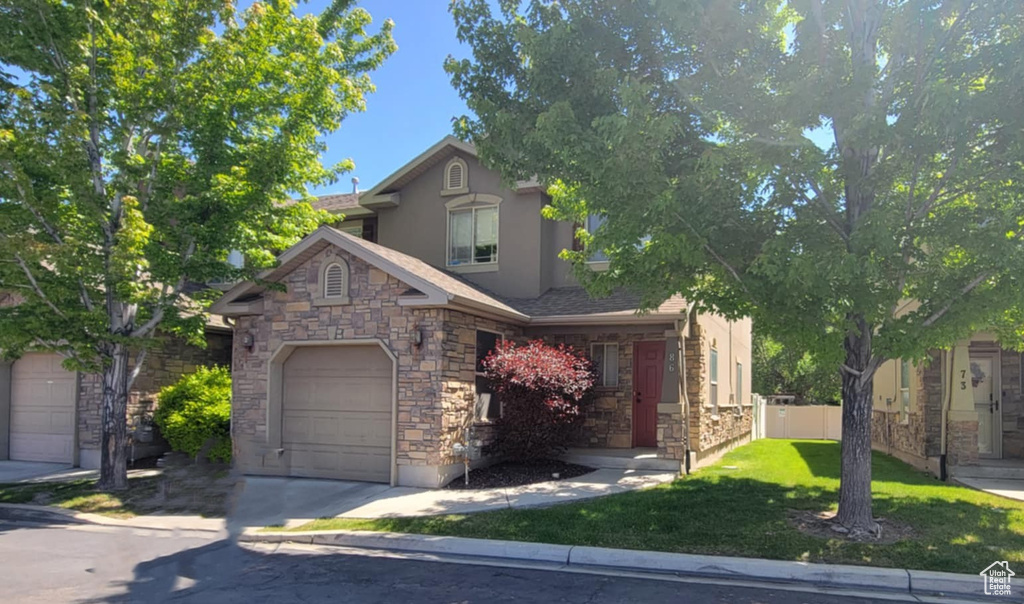 View of front facade with stucco siding, stone siding, a garage, a front lawn, and concrete driveway
