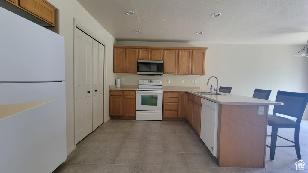 Kitchen with white appliances, a sink, a breakfast bar, a peninsula, and light countertops