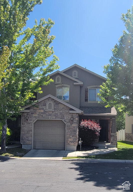 View of front of house with stone siding, stucco siding, concrete driveway, and a garage