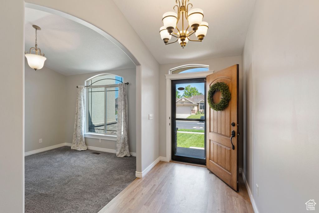 Entryway with arched walkways, a chandelier, baseboards, and light wood-style flooring