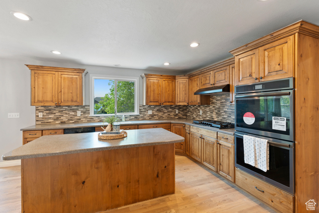 Kitchen with double oven, light wood finished floors, backsplash, a center island, and recessed lighting