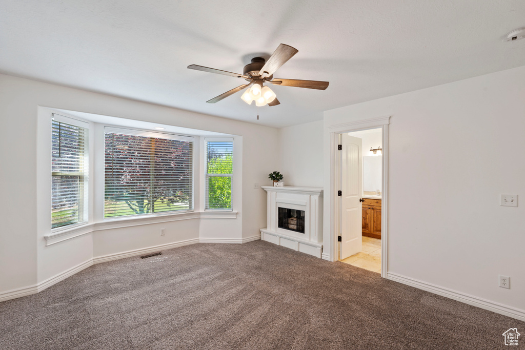Unfurnished living room featuring carpet floors, a ceiling fan, a glass covered fireplace, and baseboards